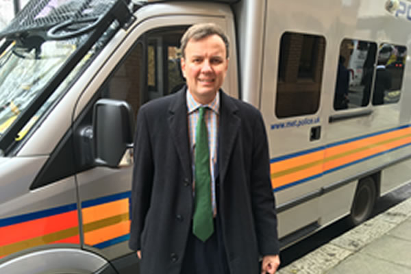 Greg Hands MP in front of a police vehicle 