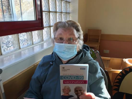 Jacqueline Narain wearing a face covering and holding a Covid-19 vaccination information booklet
